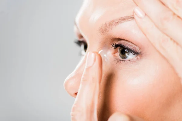 Selective focus of beautiful woman attaching contact lens isolated on grey — Stock Photo