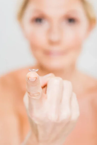 Селективный фокус контактных линз, удерживаемых зрелой женщиной, изолированный на сером — стоковое фото