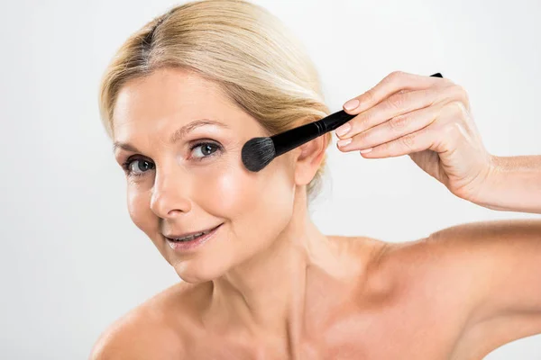 Beautiful and mature woman applying blush with cosmetic brush and looking at camera — Stock Photo