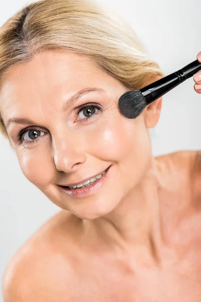 Beautiful and smiling woman applying blush with cosmetic brush and looking at camera — Stock Photo