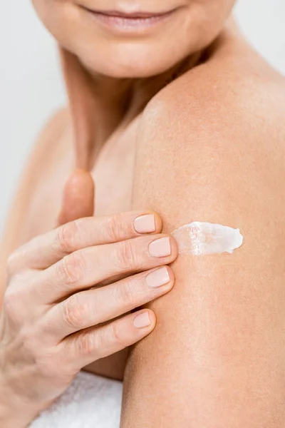 Selective focus of mature woman applying cosmetic cream  isolated on grey — Stock Photo