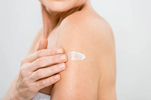 Selective focus of mature woman applying cosmetic cream isolated on grey — Stock Photo