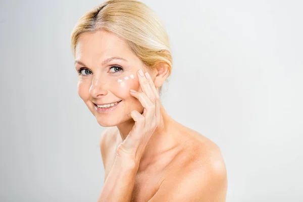 Hermosa y madura mujer mirando a la cámara y la aplicación de crema cosmética en la cara - foto de stock