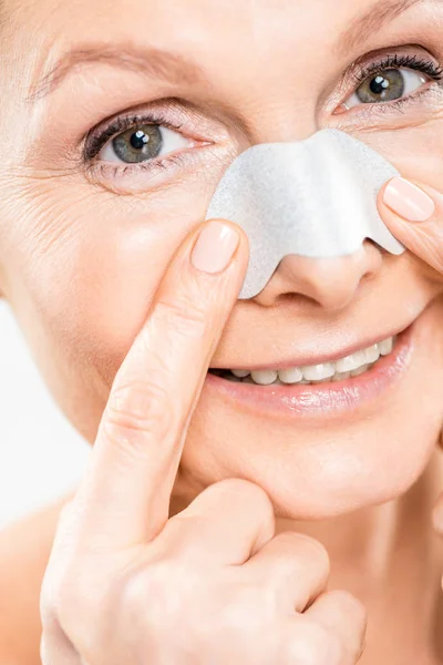 Close up de mulher bonita e madura olhando para a câmera com tira de nariz isolado no branco — Fotografia de Stock