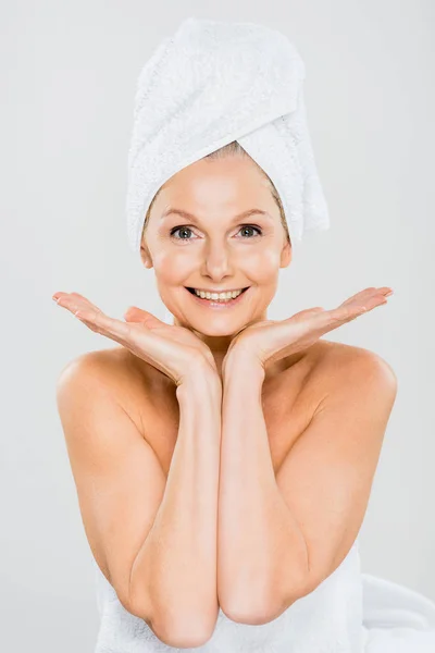 Atractiva y sonriente mujer madura en toallas mirando a la cámara aislada en gris - foto de stock