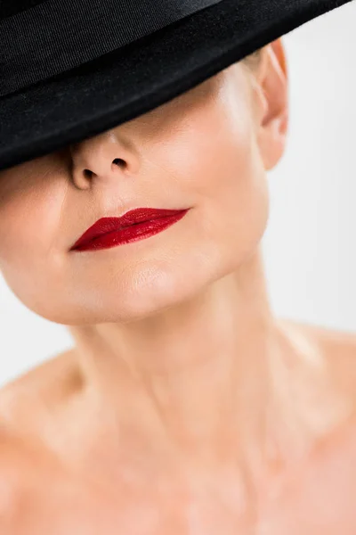 Enfoque selectivo de la mujer de mediana edad elegante y de moda con labios rojos en sombrero negro aislado en gris - foto de stock