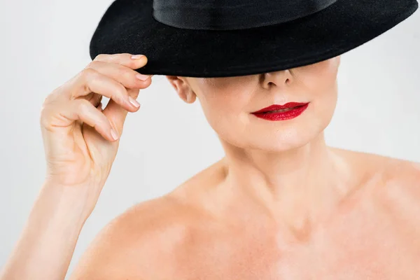 Middle aged elegant and fashionable woman with red lips touching black hat isolated on grey — Stock Photo