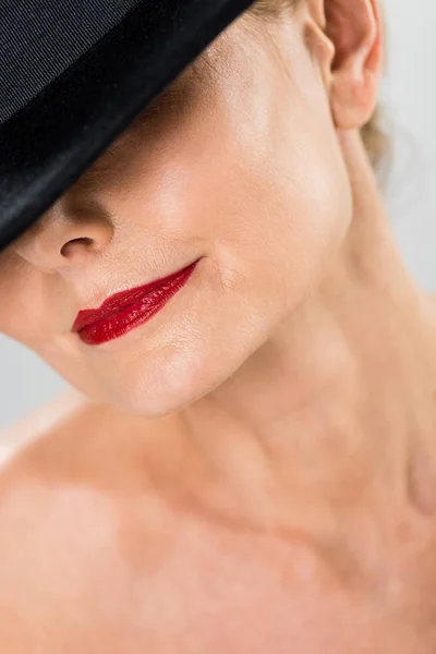 Enfoque selectivo de la mujer de mediana edad elegante y de moda con labios rojos en sombrero negro aislado en gris - foto de stock