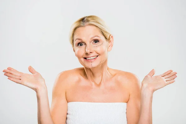 Belle femme d'âge moyen et avec des lignes sur le visage regardant la caméra et montrant un geste d'haussement d'épaules isolé sur blanc — Photo de stock