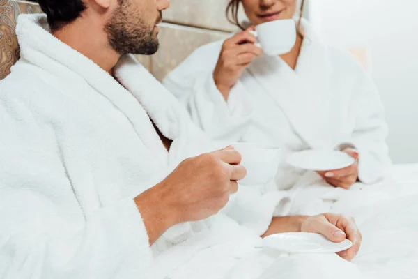 Vista recortada de hombre barbudo y novia sosteniendo tazas con café en la cama - foto de stock