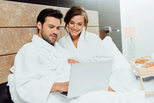 Fröhliche Frau schaut auf Laptop mit hübschem Freund im Bett — Stockfoto