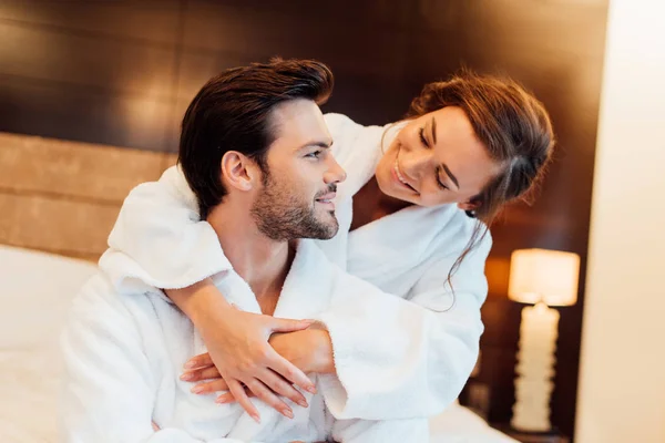 Namorada feliz em roupão de banho branco abraçando namorado bonito — Fotografia de Stock