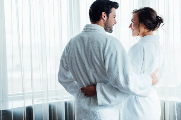 Hombre barbudo feliz abrazándose con novia bonita mientras está de pie en el hotel - foto de stock