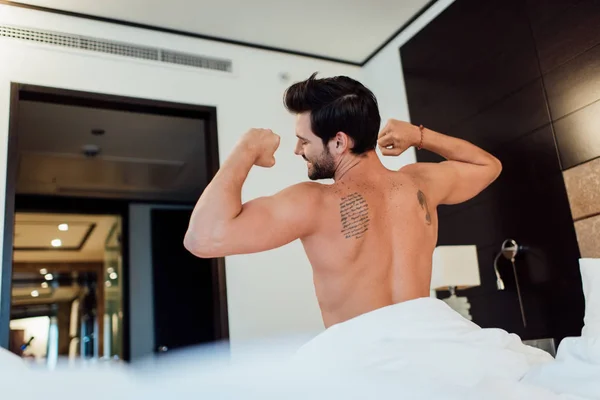 Foco seletivo do homem tatuado esticando na cama após acordar — Fotografia de Stock