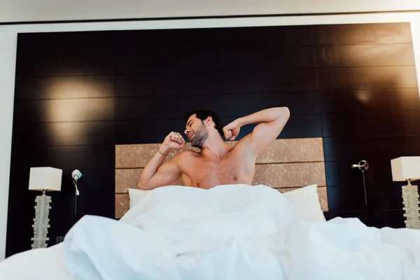 Schöner muskulöser Mann dehnt sich im Bett nach dem Aufwachen im Hotel — Stockfoto