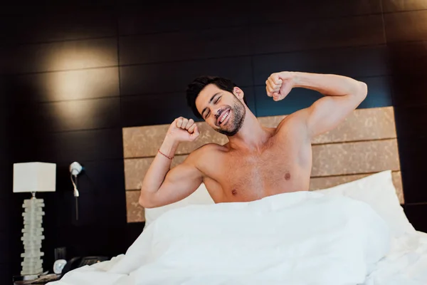 Homem muscular alegre esticando na cama depois de acordar — Fotografia de Stock