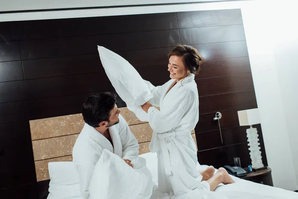 Feliz pareja teniendo almohada lucha en cama en hotel - foto de stock