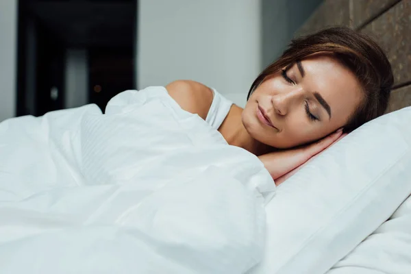 Hermosa mujer morena durmiendo en la almohada bajo la manta en la cama - foto de stock