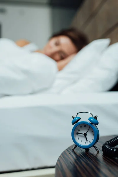 Foco seletivo de retro relógio de alarme azul perto de mulher dormindo na cama — Fotografia de Stock