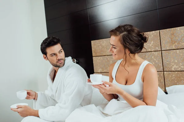 Bonito barbudo homem e bela mulher olhando para o outro enquanto segurando copos — Fotografia de Stock