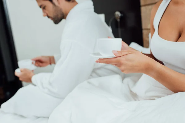 Vista recortada de la mujer y el hombre sosteniendo tazas con café en la cama - foto de stock