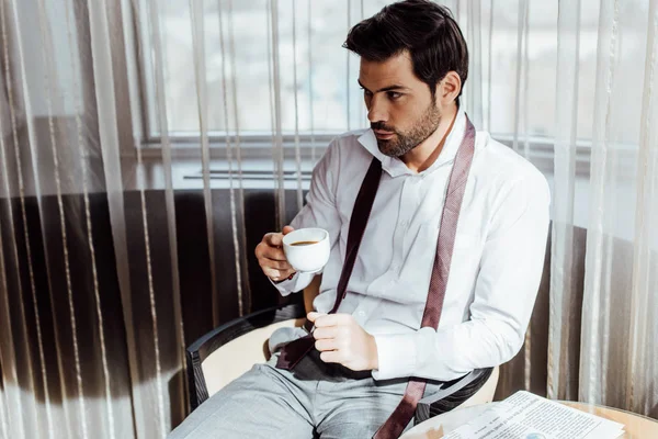 Schöner Mann im Anzug sitzt am Kaffeetisch mit Zeitung und hält eine Tasse Kaffee in der Hand — Stockfoto