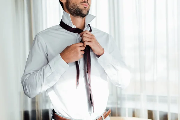 Обрезанный вид бородатого человека, трогающего галстук, стоя в отеле — стоковое фото