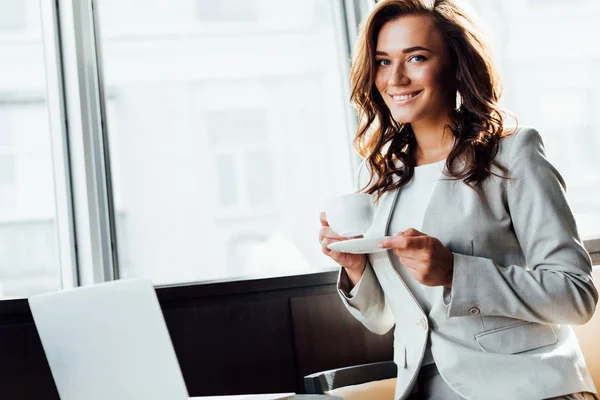Fröhliche Geschäftsfrau hält Tasse Kaffee in der Hand und blickt in die Kamera — Stockfoto