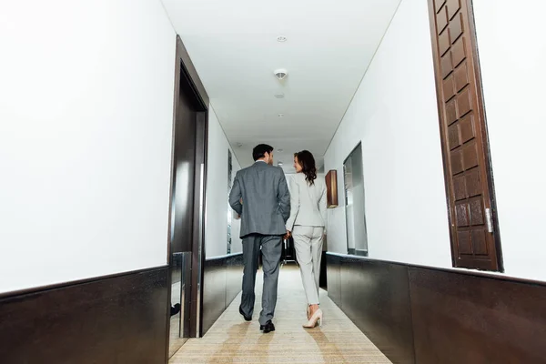 Confident businessman businesswoman in formal wear holding hands and walking in hotel corridor — Stock Photo