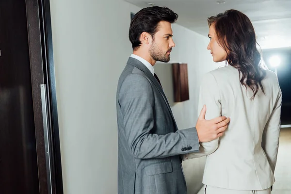 Homme d'affaires confiant toucher la main d'une femme d'affaires attrayante en tenue formelle tout en se tenant dans le couloir de l'hôtel — Photo de stock