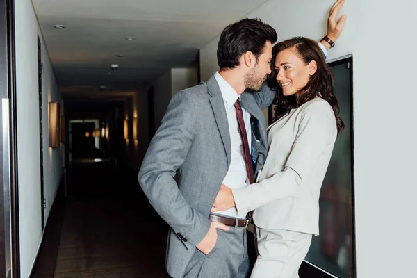 Handsome man in suit standing with hand in pocket and looking at beautiful woman in hotel corridor — Stock Photo