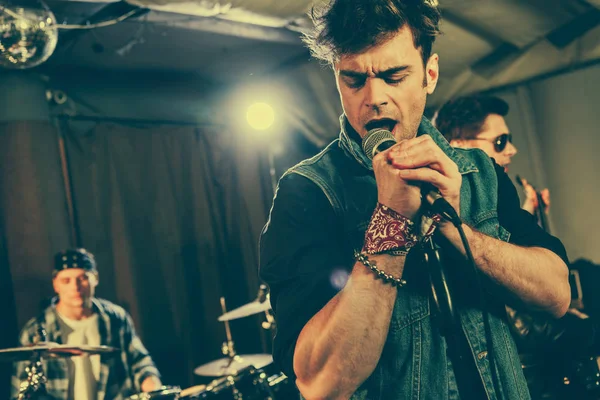 Foco seletivo do homem cantando música com banda de rock se apresentando no palco — Fotografia de Stock