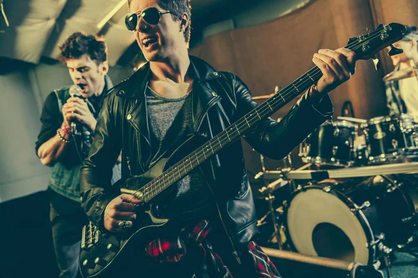 Enfoque selectivo de guitarrista alegre en gafas de sol tocando guitarra eléctrica cerca de banda de rock - foto de stock