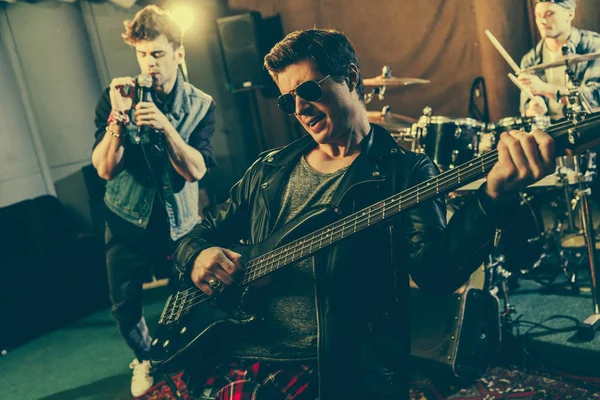 Избирательное внимание модного гитариста в солнцезащитных очках, играющего на электрогитаре рядом с рок-группой — стоковое фото