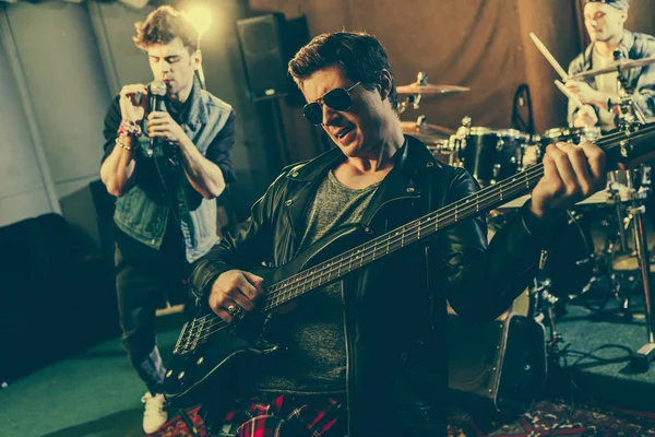 Foyer sélectif du guitariste branché dans les lunettes de soleil jouant de la guitare électrique près du groupe de rock — Photo de stock