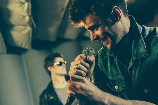 Selective focus of happy singer standing with microphone near rock band — Stock Photo