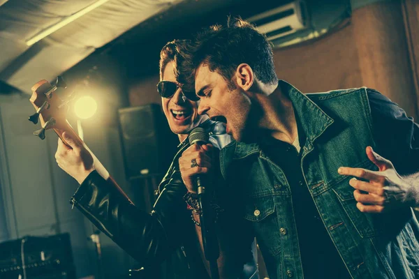 Elegante cantante cantando en micrófono con guapo guitarrista en gafas de sol — Stock Photo