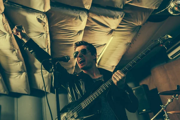 Guitarrista guapo cantando canción en micrófono mientras sostiene la guitarra electica - foto de stock