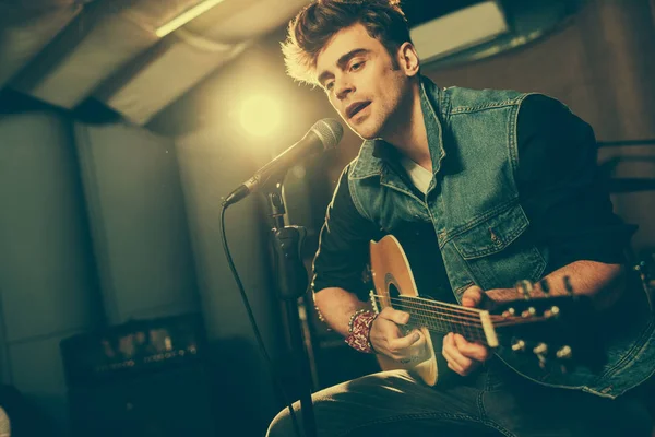 Handsome singer singing in microphone while playing acoustic guitar — Stock Photo