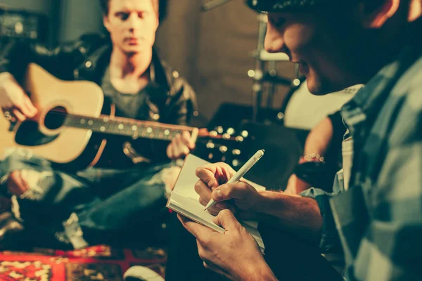 Foyer sélectif de l'écriture de compositeur joyeux dans le cahier ami proche jouant de la guitare acoustique — Photo de stock