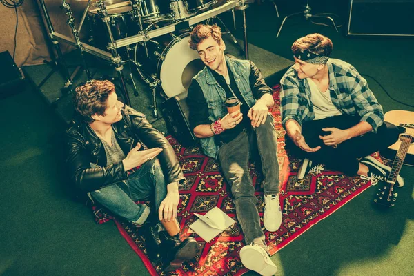 Overhead view of happy rock band talking while sitting on carpet near musical instruments — Stock Photo