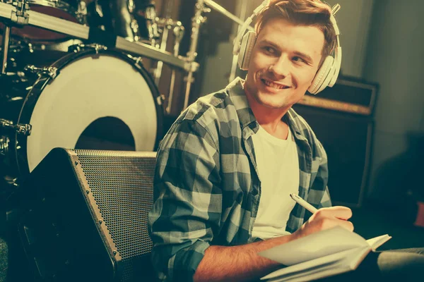 Happy young composer listening music in headphones while writing in notebook — Stock Photo