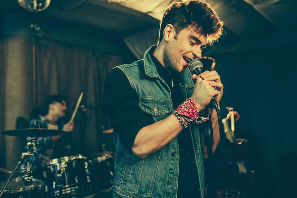 Foyer sélectif du chanteur à la mode chantant dans le microphone près du groupe de rock — Photo de stock