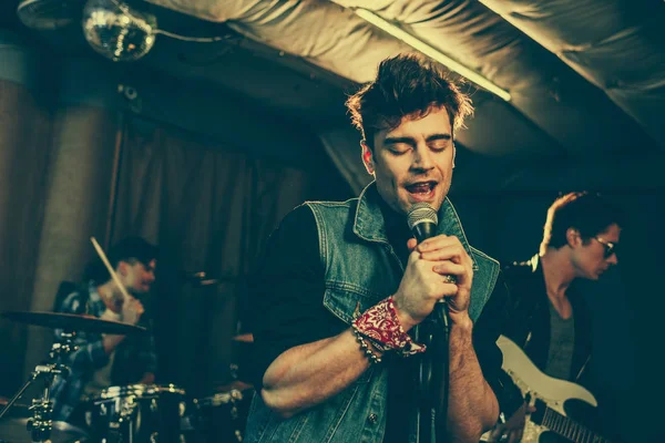 Foyer sélectif de l'homme à la mode chantant dans le microphone près du groupe de rock — Photo de stock