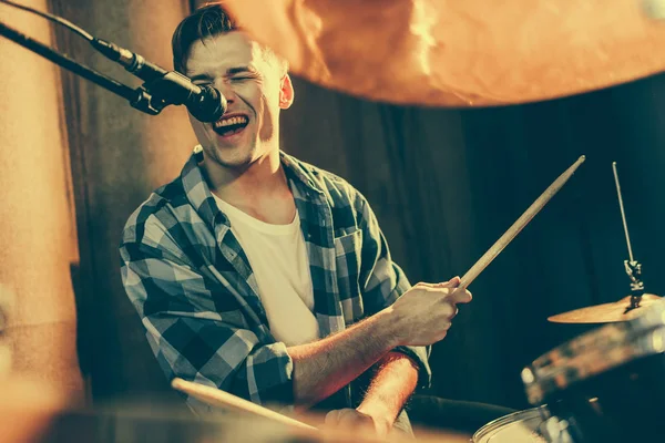 Foco seletivo de homem bonito cantando em microfone enquanto toca bateria — Fotografia de Stock