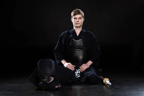 Beau jeune homme en armure kendo assis sur noir — Photo de stock