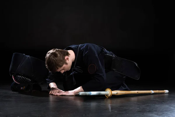 Kendo combattente con spada e casco inchinandosi sul pavimento su nero — Foto stock