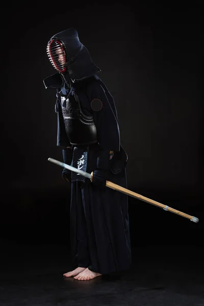 Vista completa de kendo fighter con espada inclinándose sobre negro - foto de stock