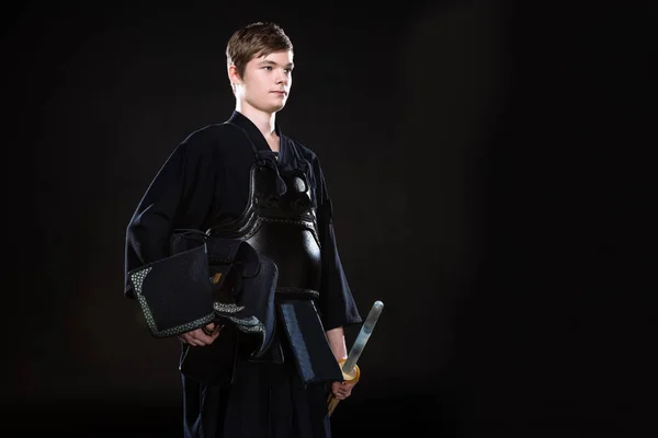 Молодий чоловік тримає кендо шолом і бамбуковий меч на чорному — стокове фото