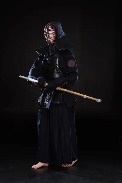 Vista completa de kendo fighter en casco sosteniendo espada de bambú sobre negro - foto de stock